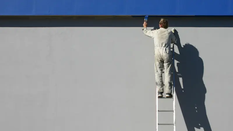 Maler in Basel: Malerin auf einer Leiter streicht eine weisse Innenwand mit dem Roller